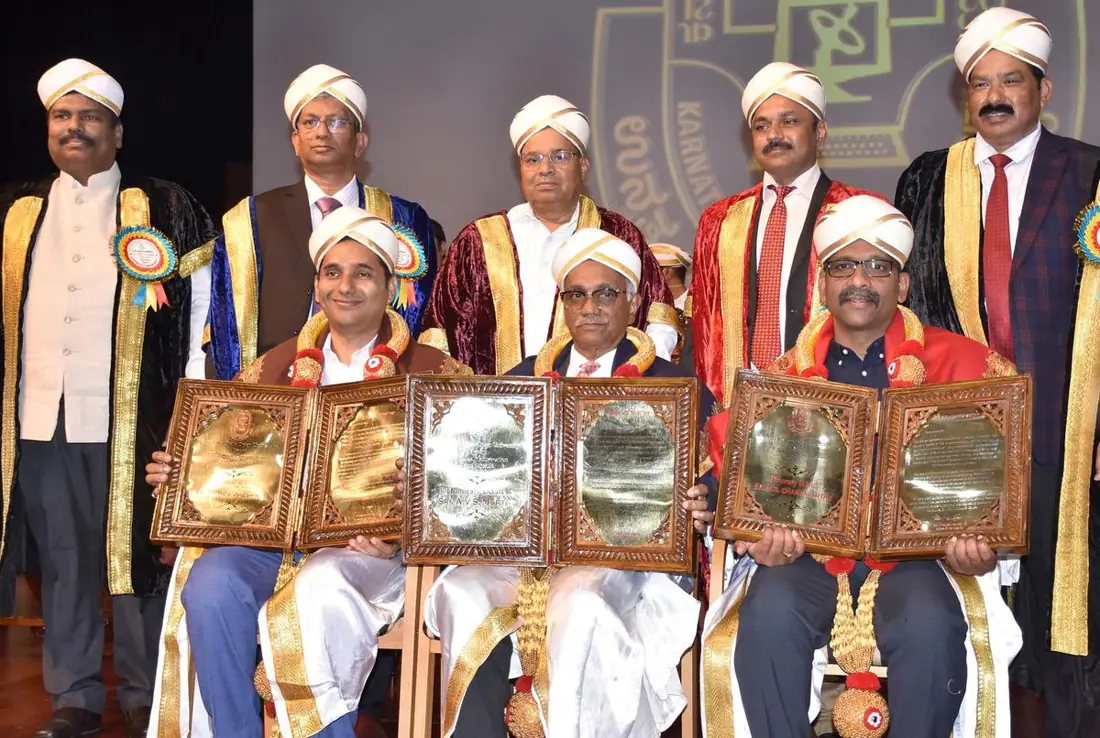 Men in academic robes and turbans holding awards at a KSOU convocation.